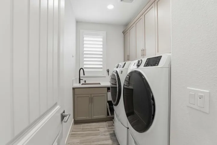 Upstairs laundry room featuring built-in cabinetry, a utility sink, and sleek modern finishes.