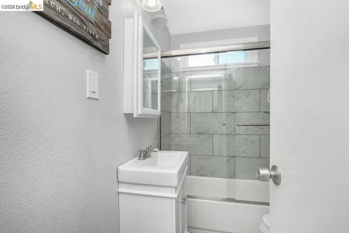 Bathroom featuring vanity, bath / shower combo with glass door, and a textured wall