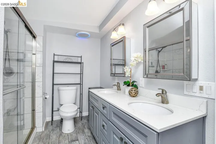 Full bath featuring double vanity, a stall shower, and light wood finished floors