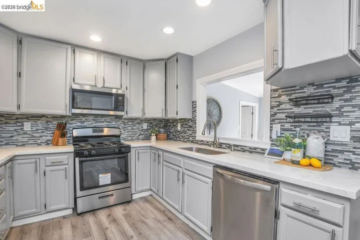 Kitchen featuring gray cabinets, stainless steel appliances, light stone counters, light wood-type flooring, and recessed lighting