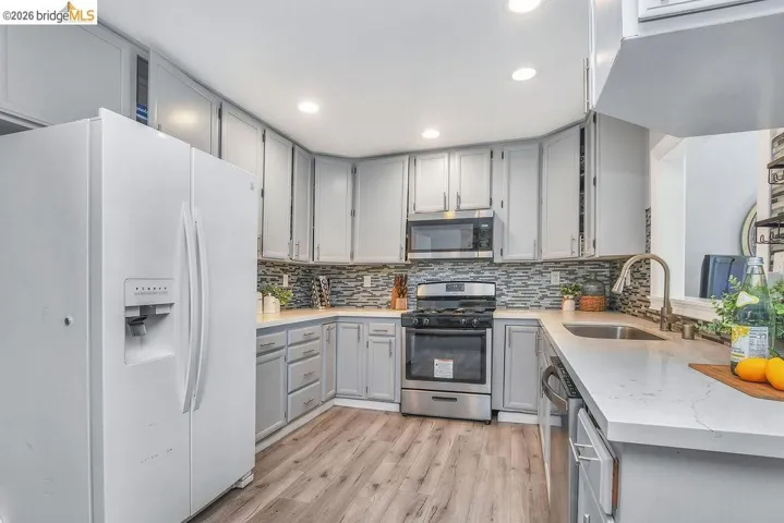 Kitchen featuring gray cabinets, stainless steel appliances, light wood finished floors, light stone countertops, and recessed lighting