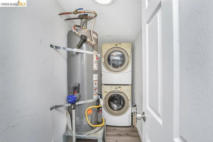 Laundry area featuring secured water heater, stacked washing machine and dryer, wood finished floors, and a textured wall