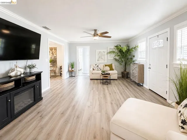 Spacious living area featuring light wood-finish flooring, light gray walls, white crown molding, and a ceiling fan