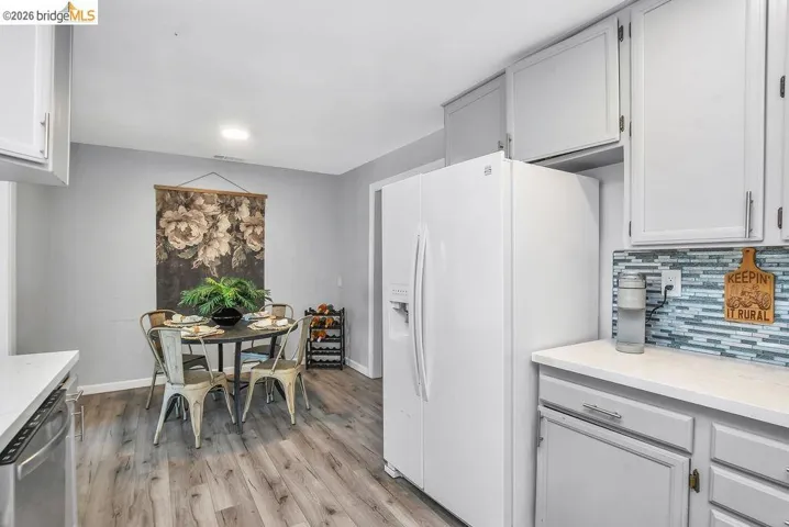 Kitchen with white fridge with ice dispenser, stainless steel dishwasher, backsplash, light wood finished floors, and white cabinetry