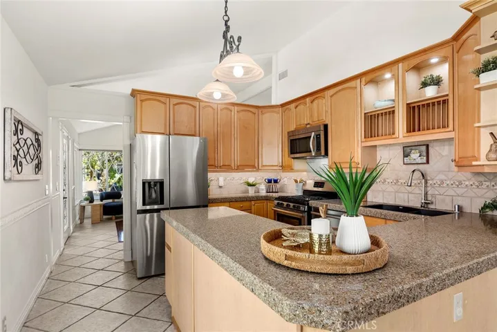 Warm, welcoming kitchen with plenty of cabinetry, including display space for your favorite plates or glassware. It also includes a stainless-steel refrigerator, tile flooring, and under-cabinet lighting—making it a great spot to gather with family and friends while cooking something extra yummy.