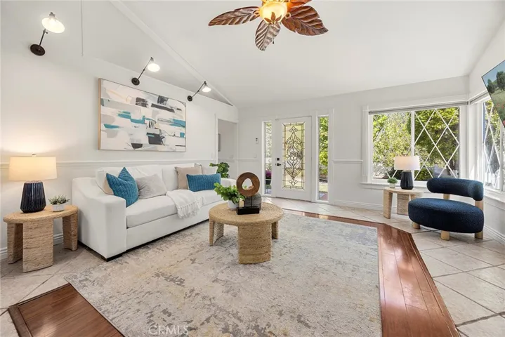 The living room featuring modern wall-mounted accent lighting, vaulted ceilings, and tile flooring with a wood inlay that adds warmth and character.