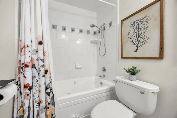 Hall bath with jetted tub and shower combo, tile surround, decorative accent detail, and modern black hardware accents.