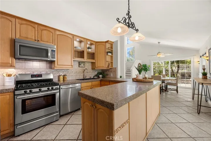Updated kitchen with stainless steel appliances, ample cabinetry, granite countertops, and a peninsula with pendant lighting, open to the dining area and has a double-pane sliding glass door with easy access to the side yard