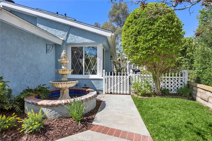 Inviting front entry with a charming fountain, white picket gate, and lush greenery creating a warm first impression.