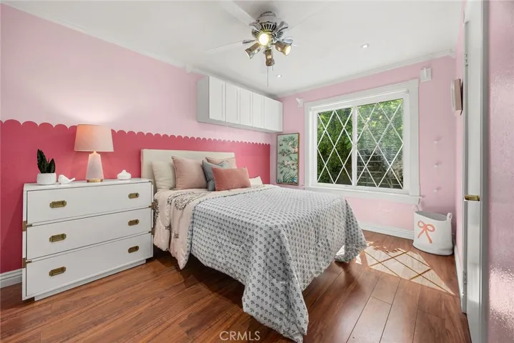 Sweet and stylish girls’ room with crown molding, laminate flooring, and a closet featuring built-ins for easy organization, plus a round wall-mounted jewelry holder for a fun and functional touch.