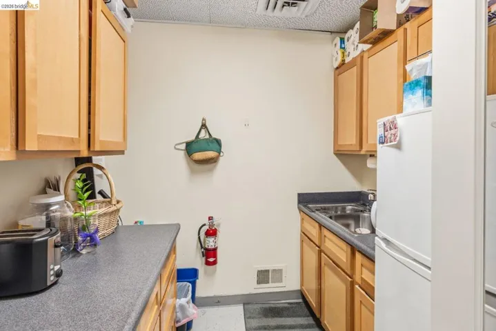 Kitchen with light wood finish cabinetry, freestanding refrigerator, dark countertops, and a textured ceiling