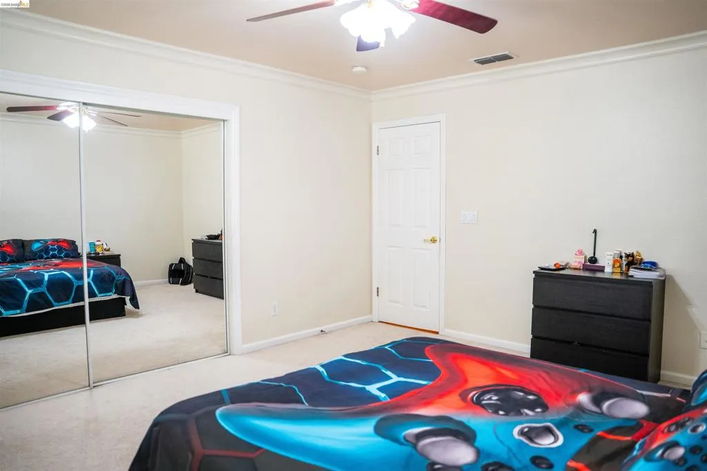 Bedroom featuring light carpet, ceiling fan, a closet, and ornamental molding