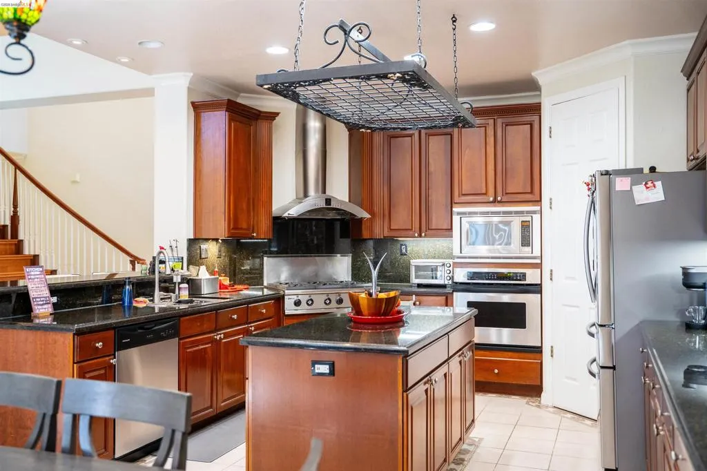 Kitchen featuring stainless steel appliances, a center island, light tile patterned flooring, decorative backsplash, and dark stone countertops