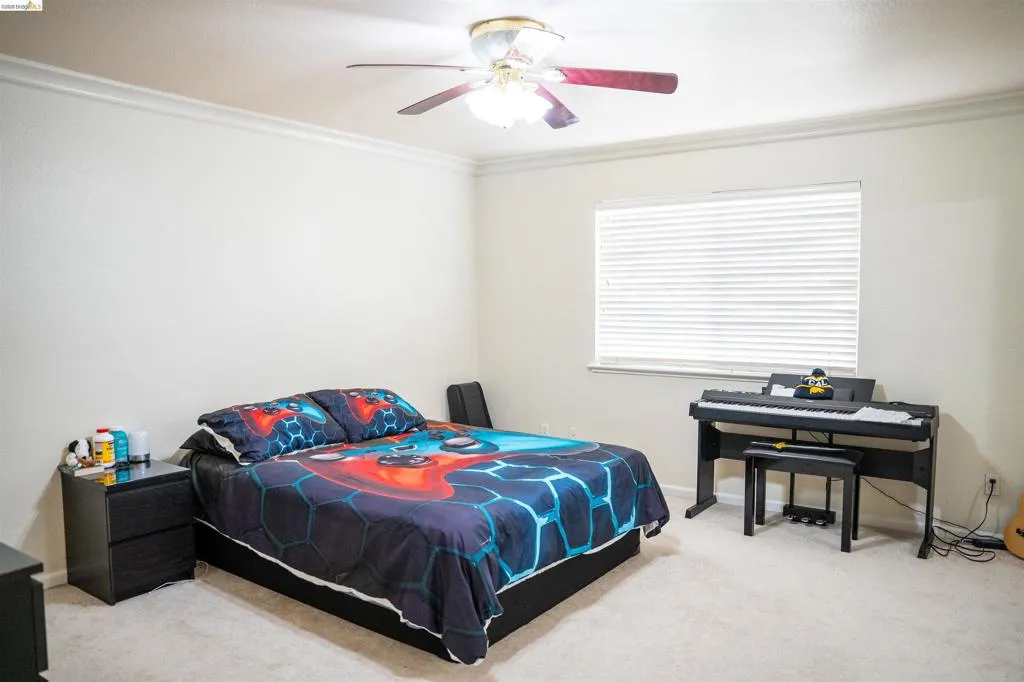 Bedroom with light colored carpet, a ceiling fan, and crown molding