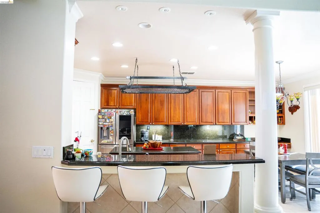 Kitchen featuring a kitchen bar, decorative columns, decorative backsplash, a peninsula, and stainless steel fridge