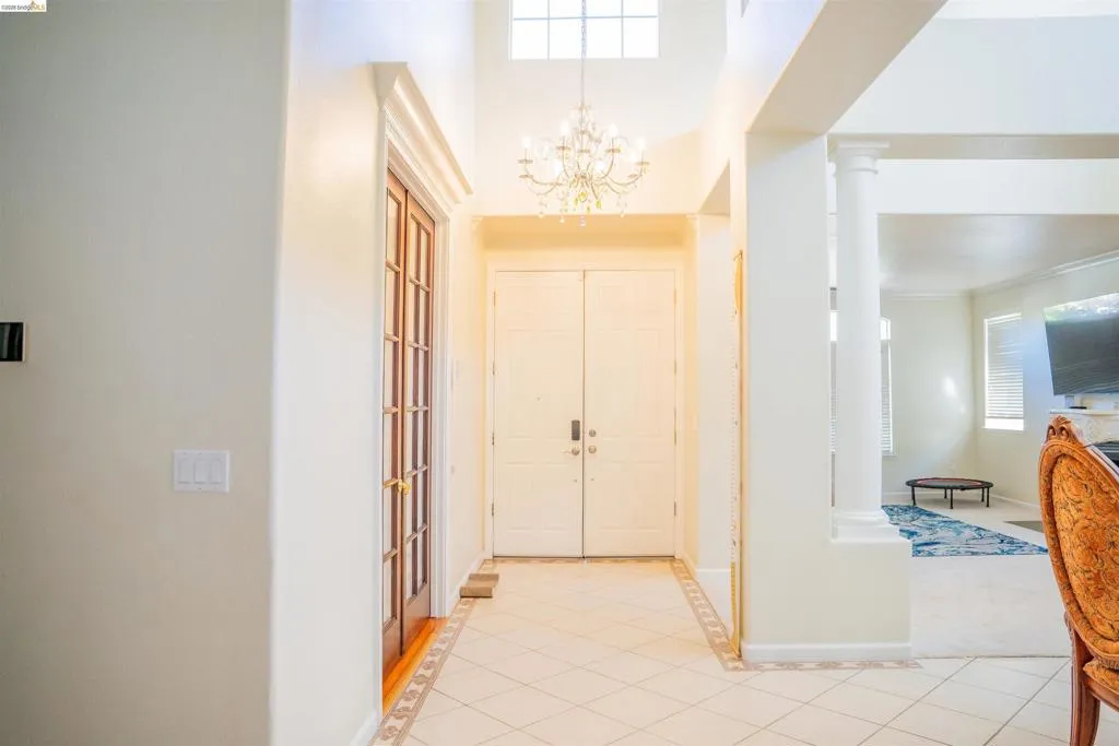 Foyer entrance featuring decorative columns, suspended lighting, light tile patterned floors, inlaid floor details, and a high ceiling