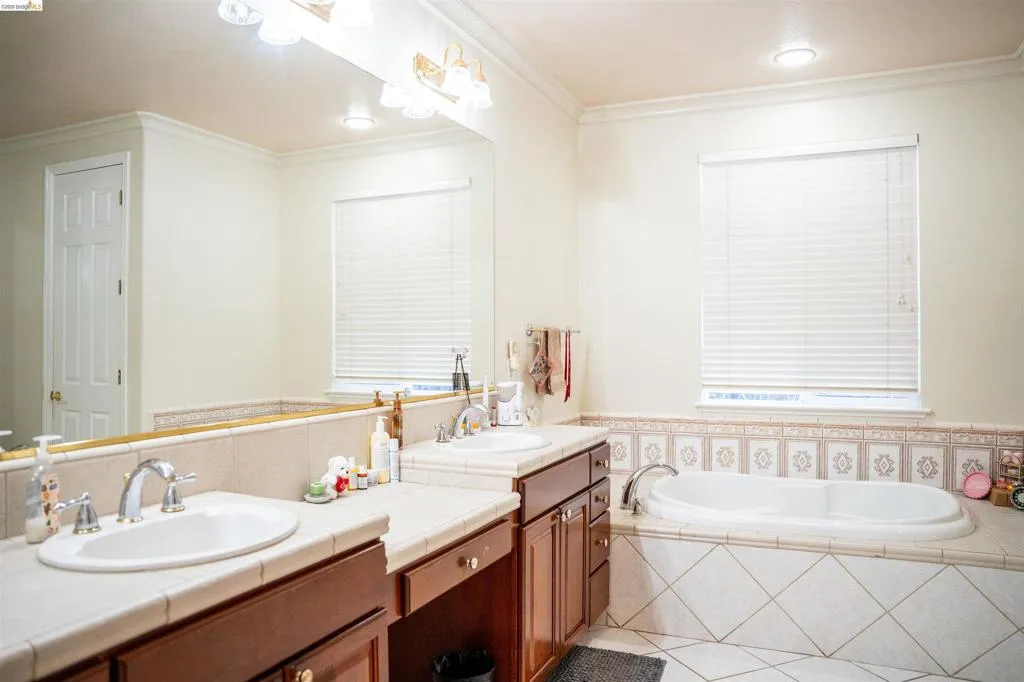 Full bath with a bath, double vanity, crown molding, and light tile patterned flooring