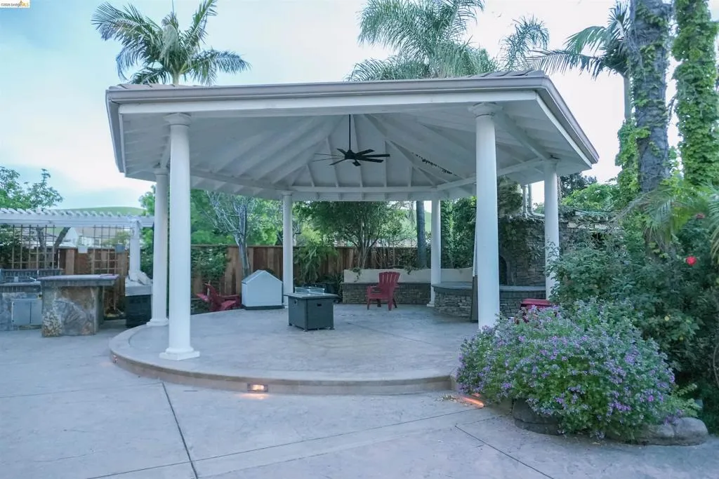 Fenced backyard featuring a gazebo, a ceiling fan, a patio area, an outdoor fire pit, and an outdoor bar