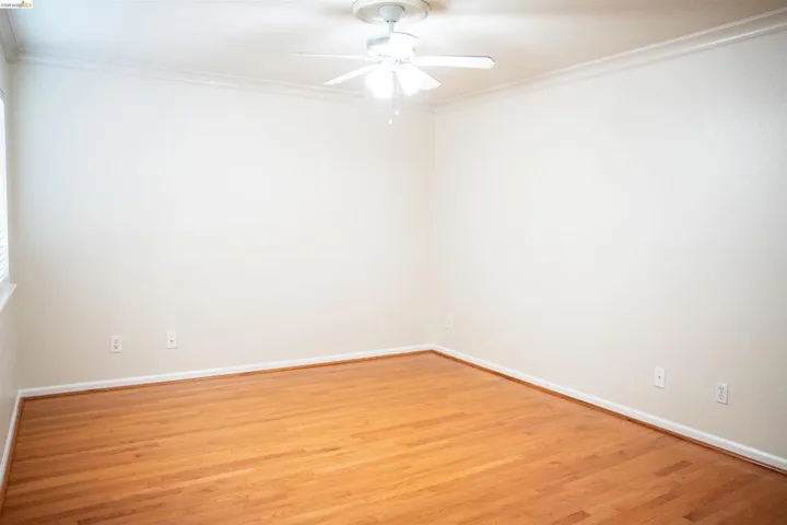 Empty room featuring light wood-style floors, ceiling fan, and ornamental molding