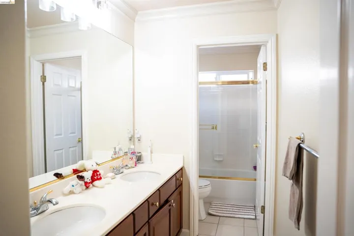 Bathroom with double vanity, ornamental molding, light tile patterned flooring, and enclosed tub / shower combo