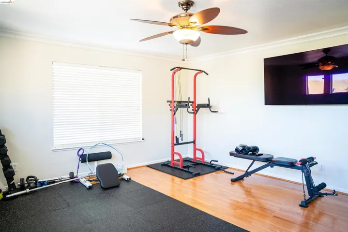 Workout room with ceiling fan, wood finished floors, and ornamental molding