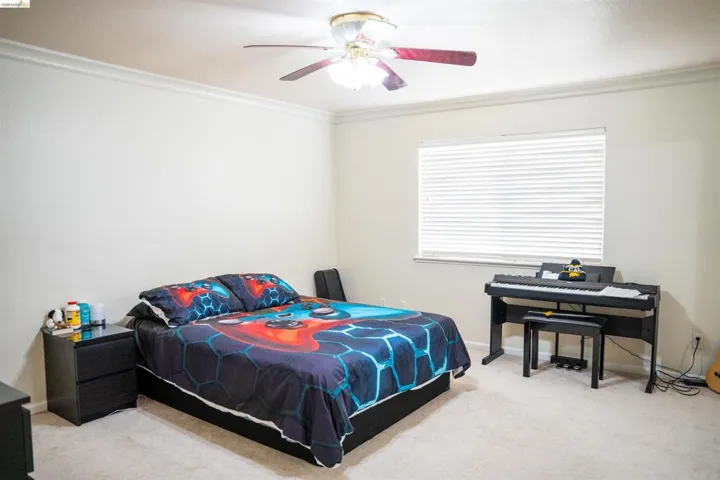 Bedroom with light colored carpet, a ceiling fan, and crown molding