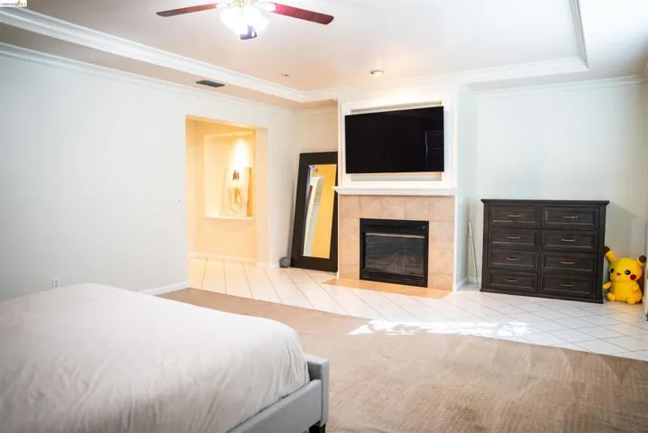 Bedroom with light tile patterned floors, ornamental molding, a tiled fireplace, and ceiling fan