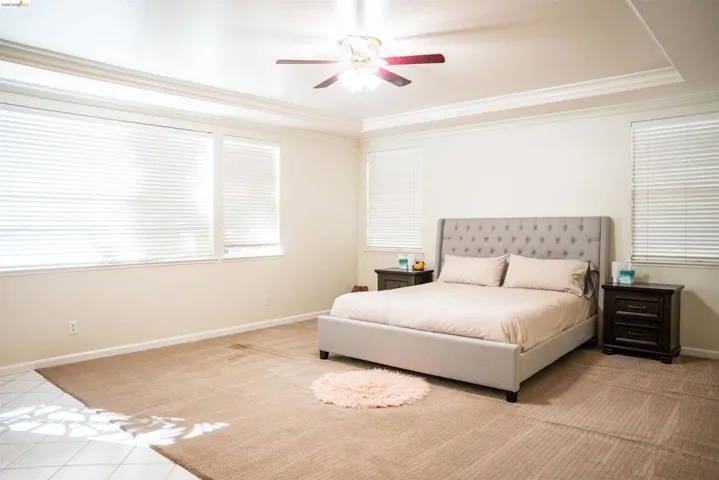 Bedroom featuring crown molding, ceiling fan, a tray ceiling, and light tile patterned floors
