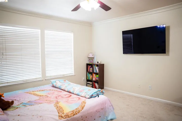 Bedroom with carpet floors, ceiling fan, and crown molding