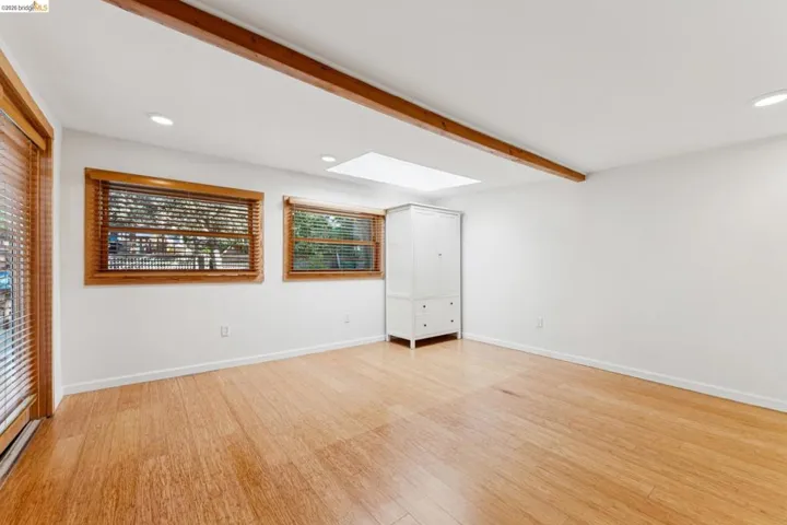Empty room featuring beamed ceiling, light wood-style floors, recessed lighting, and a skylight.