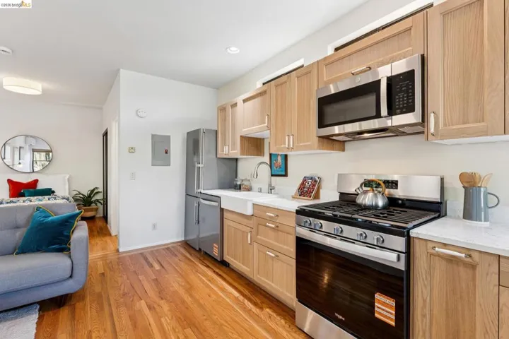 Kitchen with open floor plan, stainless steel appliances, light wood-type flooring, light wood finish cabinets, and light stone countertops