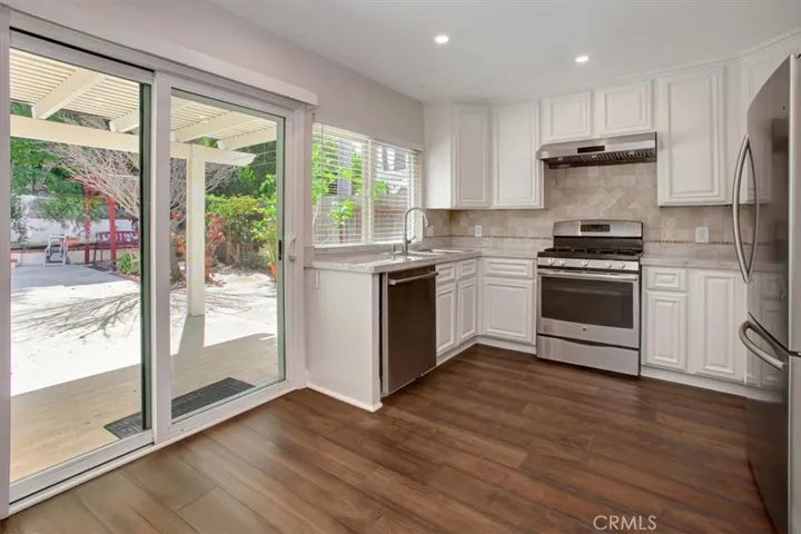 Kitchen with tile countertops, range hood, gas stove, dishwasher, recessed lighting
