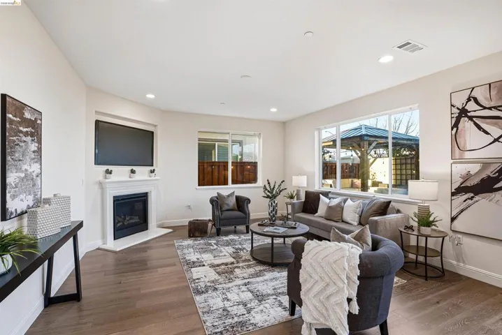 Living room with wood finished floors, a glass covered fireplace, and recessed lighting