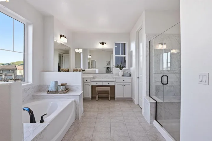 Bathroom featuring vanity, a marble finish shower, a bath, light tile patterned floors, and healthy amount of natural light