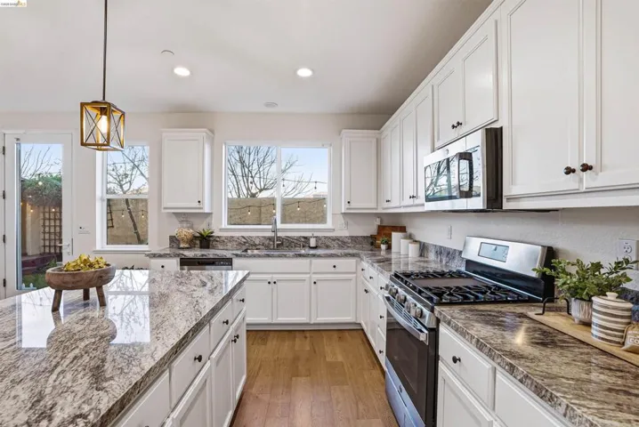 Kitchen featuring stainless steel appliances, white cabinets, light wood-style flooring, decorative light fixtures, and dark stone counters