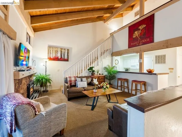 Carpeted living room with a stone fireplace and a high wood beamed ceiling