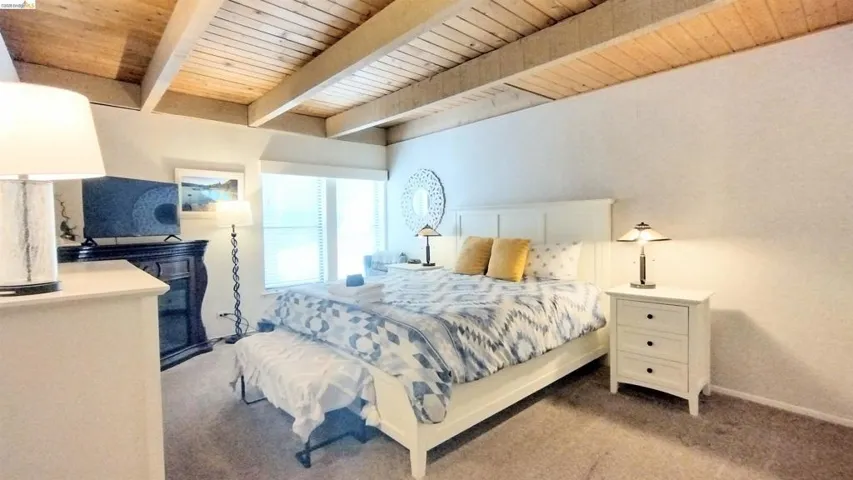 Bedroom featuring light colored carpet and a wooden ceiling with exposed beams