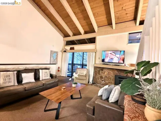 Living area featuring a fireplace, a high wooden beamed ceiling, and carpet flooring
