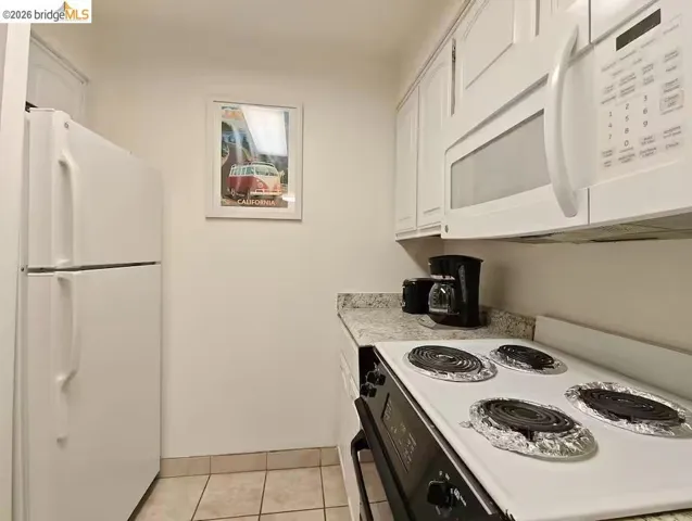 Kitchen featuring white appliances, light countertops, white cabinets, and light tile patterned floors