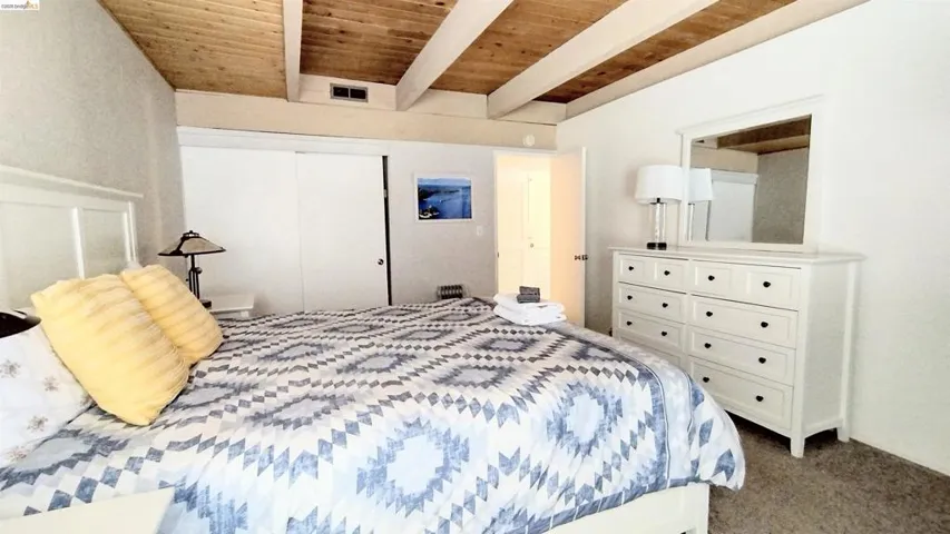 Bedroom with a wood ceiling with exposed beams, a closet, and dark carpet