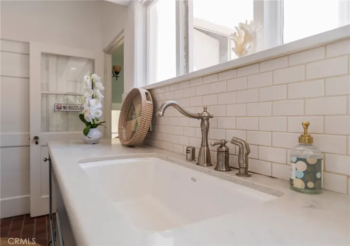 Farmhouse sink with classic fixtures, subway tile backsplash, and bright window—clean, coastal detail.