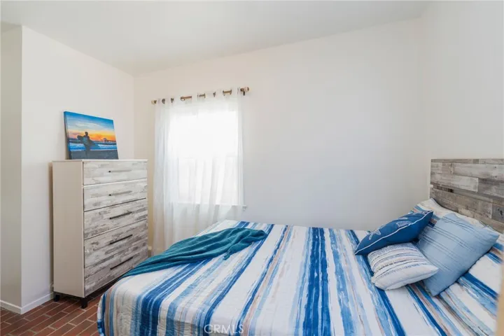 Comfortable bedroom with full bed, dresser storage, and bright natural light—simple, beachy, and inviting.