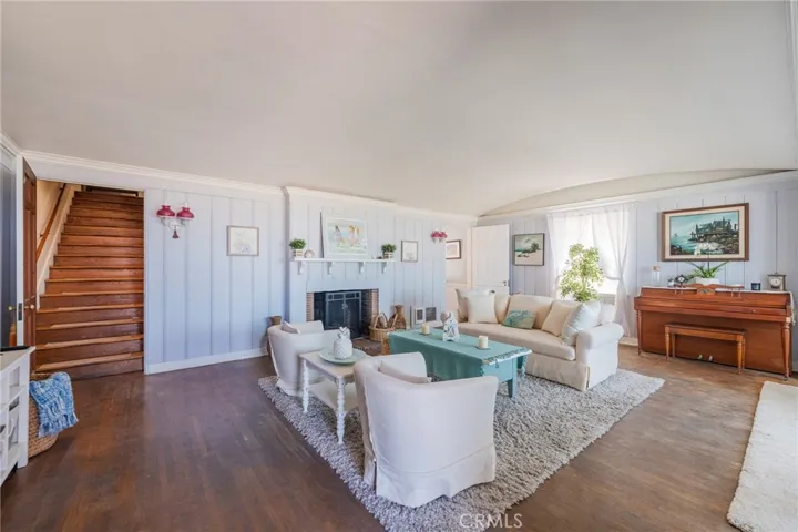 Spacious, light-filled living room with charming coastal accents, fireplace focal point, and warm wood floors. Open layout with staircase access and inviting seating area.