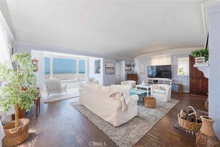 Light-filled living room with ocean-view windows, coastal décor, and warm wood floors. Spacious layout with fireplace and multiple seating areas for relaxing and entertaining.