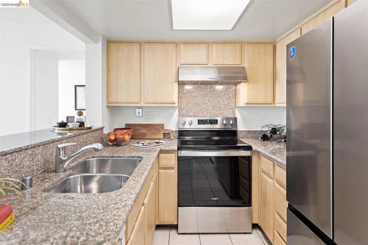 Kitchen featuring light wood finish cabinets, stainless steel appliances, light stone countertops, ventilation hood, and light tile patterned floors