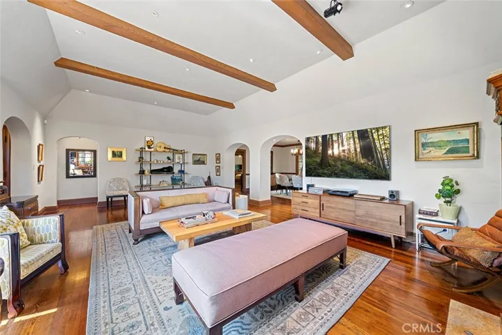 Elegant and comfortable all wrapped in this lovely living room with high beamed ceilings and lighting that is perfectly situated to complement artwork one might have. Archways to the middle right leads to the formal dining room. Standing from the fireplace area. Archway to the left side leads to the primary bedroom with en suite.