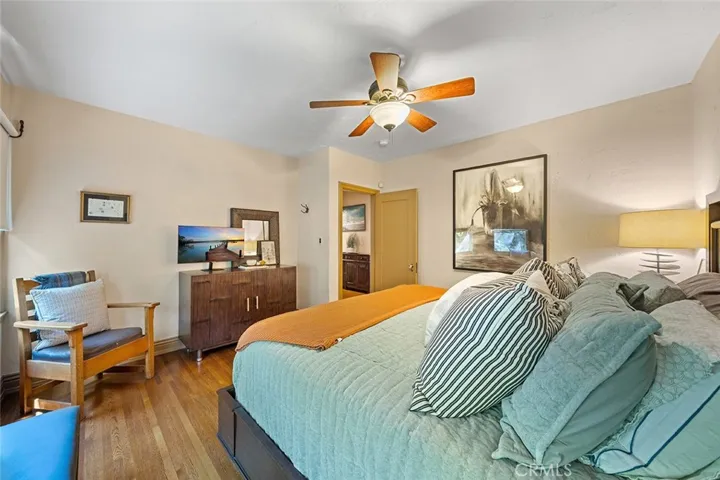 One of four bedrooms downstairs with ceiling fan and wood flooring.
