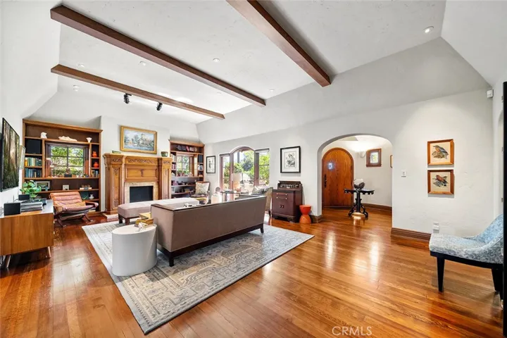 Elegance and comfort abound in this lovely living room with high beamed ceilings and perfectly placed lighting to accent any art one may have for display. Large picture window faces the front yard with privacy hedges. Formal entry in near distance at archway with wine cellar (not shown in image)