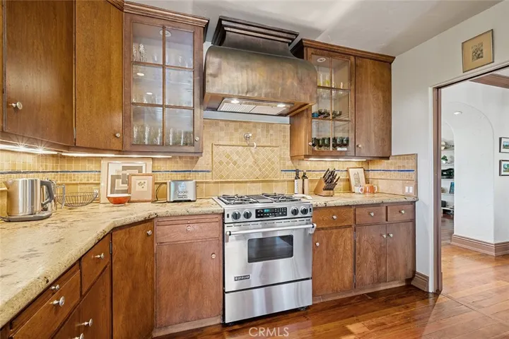 Instant pot filler above the stainless steel range with a gorgeous hood set between glass paned cupboards to place your pretty dishes. Granite counter complimented with travertine tile adds to the warmth of this kitchen.