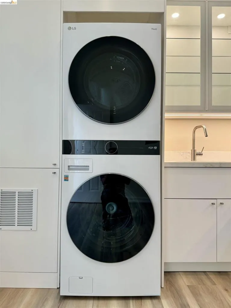 Laundry area featuring stacked washer and clothes dryer, cabinet space, and light wood-style flooring